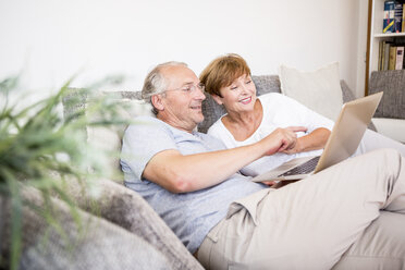 Senior couple at home sitting on couch using laptop - WESTF22746