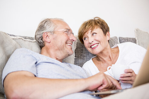 Glückliches älteres Paar sitzt zu Hause auf der Couch und benutzt einen Laptop - WESTF22747