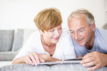 Senior couple at home lying on couch looking at photo album - WESTF22749