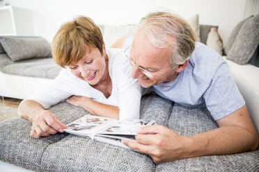 Senior couple at home lying on couch looking at photo album - WESTF22750