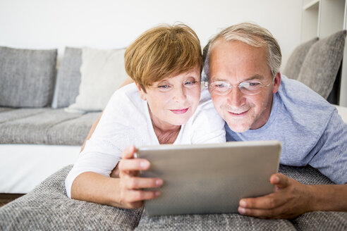 Älteres Ehepaar zu Hause auf der Couch liegend mit digitalem Tablet - WESTF22751