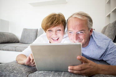 Glückliches älteres Paar, das zu Hause auf der Couch liegt und ein digitales Tablet benutzt - WESTF22752