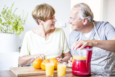 Älteres Ehepaar bereitet in der Küche frisch gepressten Orangensaft zu - WESTF22759