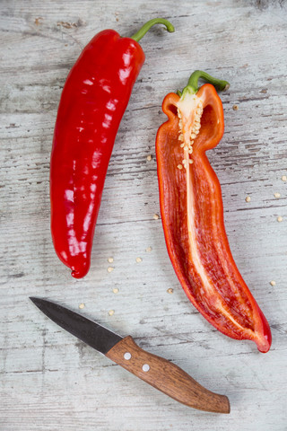Ganzer und in Scheiben geschnittener roter Spitzpaprika und ein Küchenmesser auf Holz, lizenzfreies Stockfoto