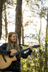 Glückliche junge Frau spielt Gitarre in der Natur - KKAF00413