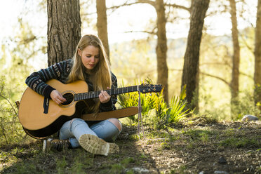 Young woman playing guitar in nature - KKAF00415