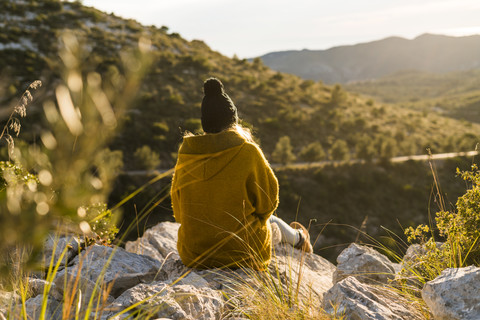 Junge Frau sitzt auf einem Felsen in der Natur und betrachtet die Aussicht, lizenzfreies Stockfoto