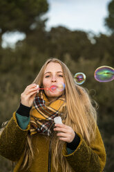 Portrait of young woman blowing soap bubbles in nature - KKAF00429