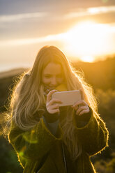 Junge Frau in der Natur nimmt ein Selfie bei Sonnenuntergang - KKAF00434