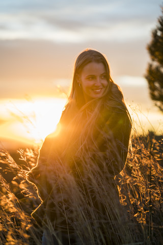 Lächelnde junge Frau in der Natur bei Sonnenuntergang, die sich umdreht, lizenzfreies Stockfoto