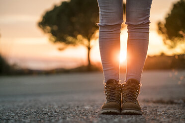 Frau in Wanderschuhen auf einer Straße bei Sonnenuntergang - KKAF00443