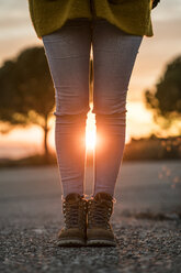 Frau in Wanderschuhen auf einer Straße bei Sonnenuntergang - KKAF00444