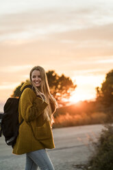 Lächelnde junge Frau in der Natur bei Sonnenuntergang, die sich umdreht - KKAF00445