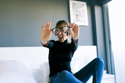 Junge Frau auf dem Bett, die ihre Brille hält - VABF01121