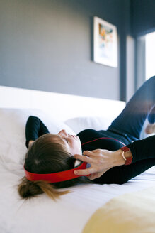 Relaxed young woman lying on bed wearing headphones - VABF01122