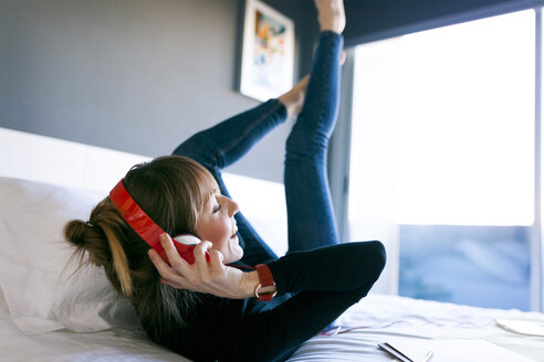 Glückliche junge Frau auf dem Bett liegend mit Kopfhörern - VABF01123