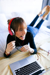 Young woman lying on bed with laptop wearing headphones - VABF01127