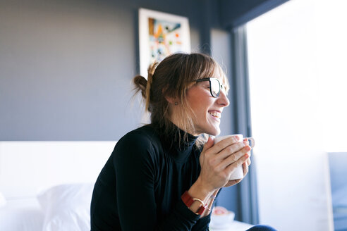 Glückliche junge Frau zu Hause beim Trinken einer Tasse Kaffee - VABF01130