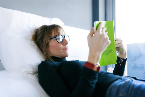 Young woman lying on bed reading a book stock photo
