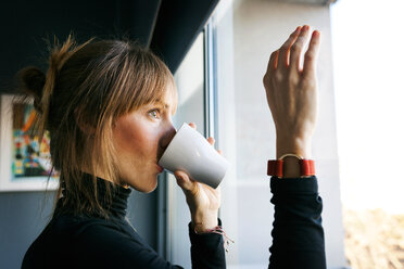 Junge Frau trinkt eine Tasse Kaffee und schaut aus dem Fenster - VABF01139