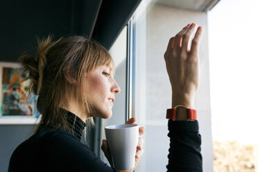 Junge Frau trinkt eine Tasse Kaffee und schaut aus dem Fenster - VABF01140
