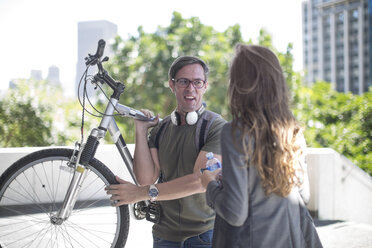 Junge Frau im Gespräch mit jungem Mann, der ein Fahrrad auf der Schulter trägt - ZEF12838