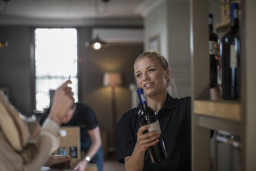 Lächelnde Verkäuferin beim Verpacken von Weinflaschen im Regal eines Weinladens - ZEF12858