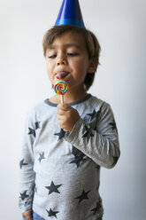 Porträt eines kleinen Jungen mit blauem Partyhut, der einen Lutscher leckt - VABF01141