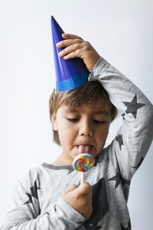 Porträt eines kleinen Jungen mit blauem Partyhut, der einen Lutscher leckt - VABF01142