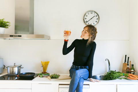 Junge Frau trinkt frischen Grapefruitsaft in ihrer Küche, lizenzfreies Stockfoto