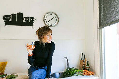Young woman drinking fresh grapefruit juice in her kitchen - VABF01164