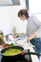 Junge Frau kocht zu Hause mit digitalem Tablet für Rezepte - VABF01169