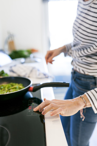 Junge Frau kocht vegane Nudeln in ihrer Küche, lizenzfreies Stockfoto