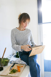 Young woman cooking at home using digital tablet for recipe - VABF01178