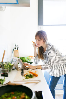 Young woman cooking at home using digital tablet for recipe - VABF01179