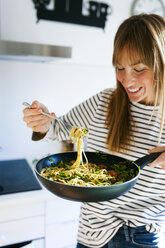 Young woman holding pan with vegan pasta dish - VABF01182