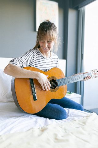 Young woman playing guitar, sitting on bed stock photo