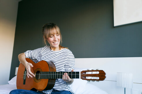 Young woman playing guitar, sitting on bed - VABF01202