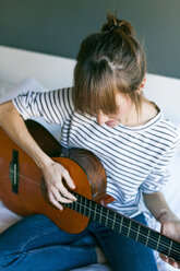 Young woman playing guitar, sitting on bed - VABF01203