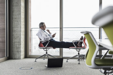 Ein leitender Angestellter im Büro sitzt auf einem Stuhl und legt die Füße hoch, um zu telefonieren - UUF09933