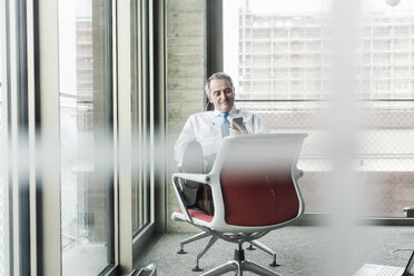 Senior manager in office sitting on chair talking on the phone - UUF09936