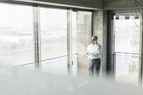 Senior manager in office standing at window, talking on the phone stock photo