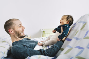 Happy father lying playing with his newborn baby girl in bed - GEMF01478