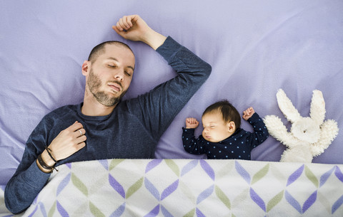 Neugeborenes Baby Mädchen, Vater und ein ausgestopftes Kaninchen schlafen im Bett, lizenzfreies Stockfoto