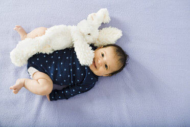 Happy newborn baby girl on bed with a stuffed rabbit - GEMF01483