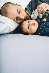 Father playing with his newborn baby girl and a a cuddly toy on bed - GEMF01485