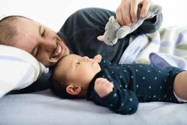 Vater spielt mit seinem neugeborenen Mädchen und einem Kuscheltier auf dem Bett - GEMF01487