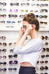 Young woman putting on sunglasses in an optician shop - LMF00619