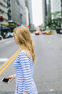 USA, New York, Manhattan, Junge Frau geht auf der Straße, hält Handy - GIOF01887