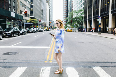 USA, New York, Manhattan, Junge Frau geht auf der Straße, hält Handy - GIOF01888